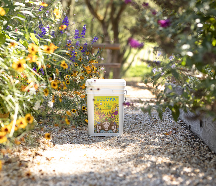 The 25-pound size of ECOMAX Neem Kernel Fertilizer surrounded by colorful plants it nourished