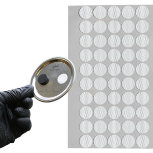 Cultivator holding up a gloved hand with jar lid with filter stuck onto it in front of a sheet of the jar lid filters.